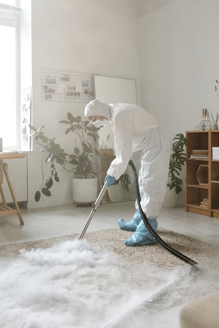 A yellow canister vacuum cleaner with a flexible hose and floor attachment resting on a decorative area rug in a living room. To the left, there is a wooden media console with a black metal frame, hol