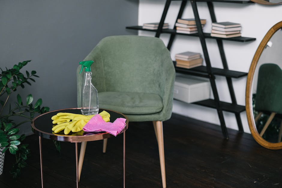 A female cleaning professional from Catford Carpet Cleaners standing in a modern living room during a domestic cleaning session. She is smiling and holding a spray bottle of cleaning solution in her r